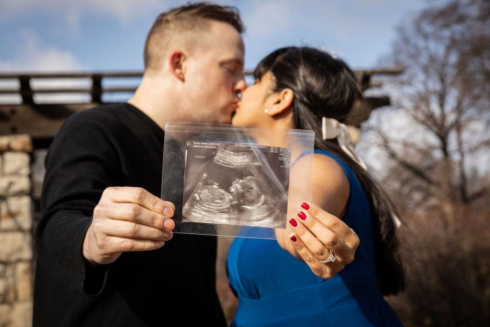 Couple shares intimate moment while holding ultrasound photo during pregnancy announcement.