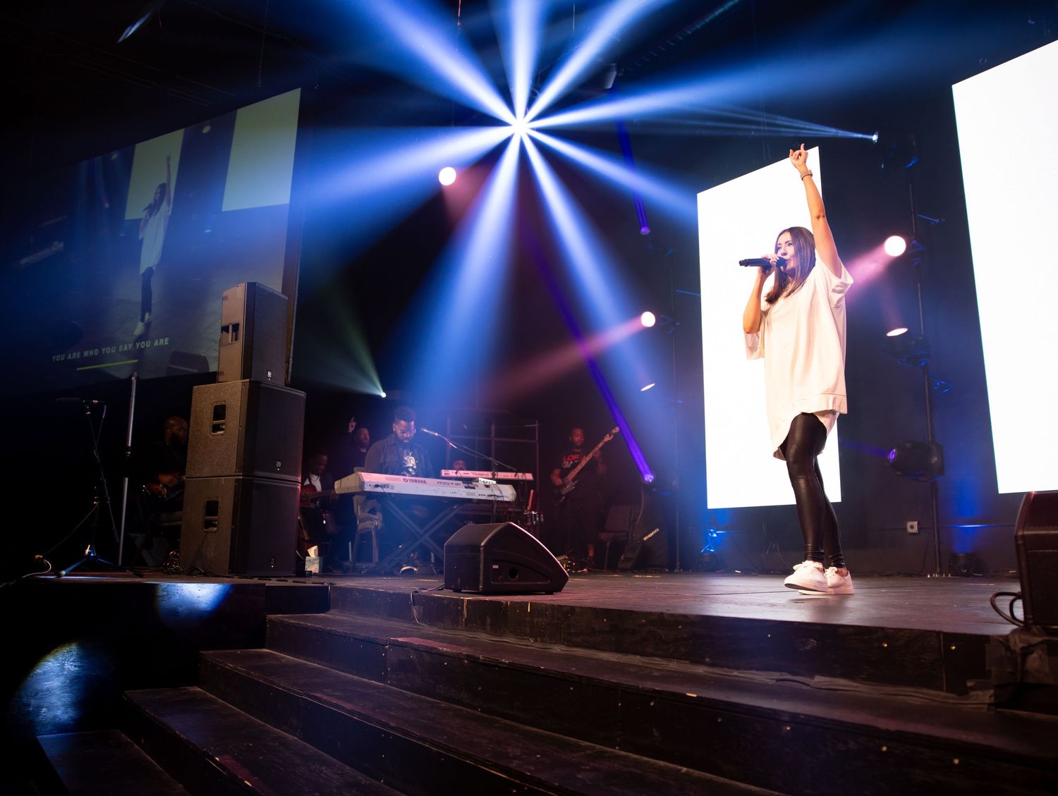 Stage performance with dramatic blue starburst lighting effects and sound equipment visible on a dark concert stage.
