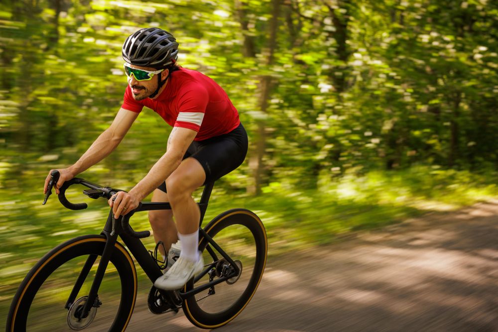 Cyclist in red jersey riding road bike through lush green forest path.