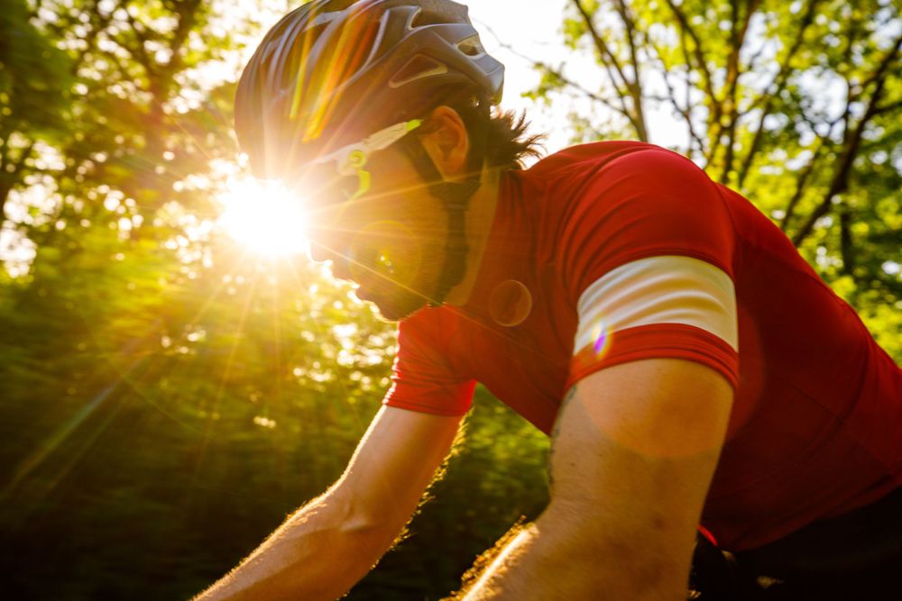 Cyclist in red jersey riding at sunset with sun flare through trees.