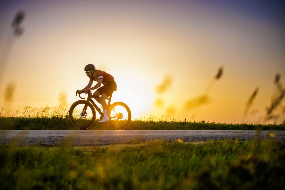 Silhouette of cyclist riding on path during dramatic sunset.