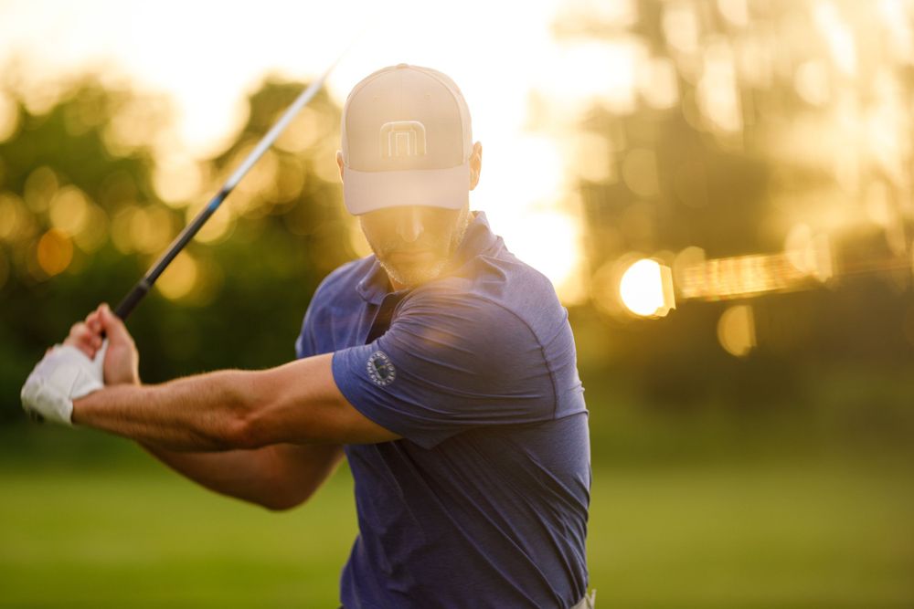 Golfer swinging club against golden sunset sky.
