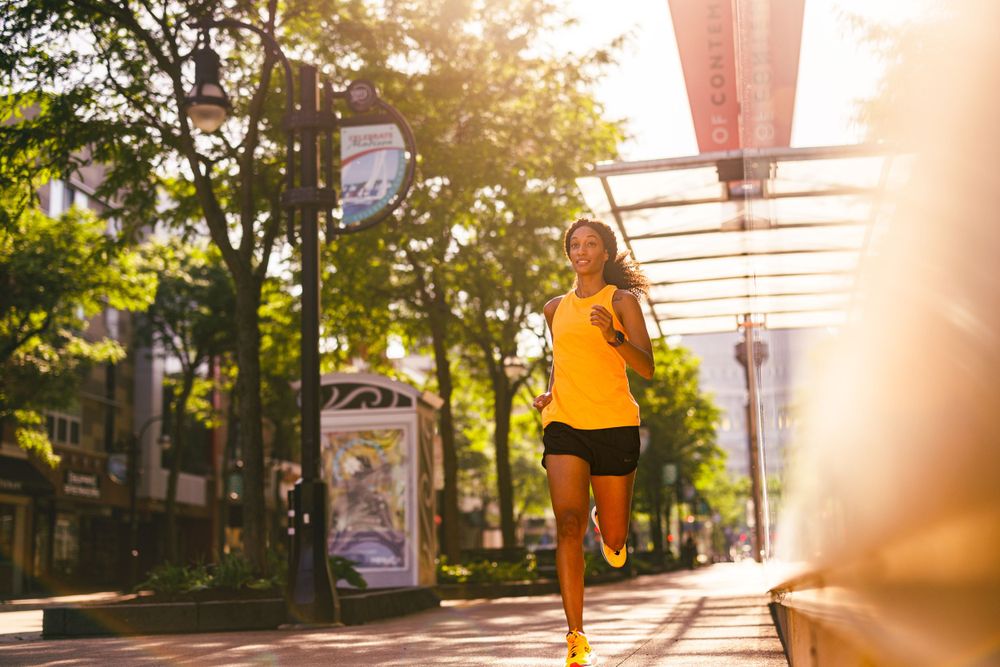 Person in yellow athletic wear running along sidewalk under covered pathway during sunrise.