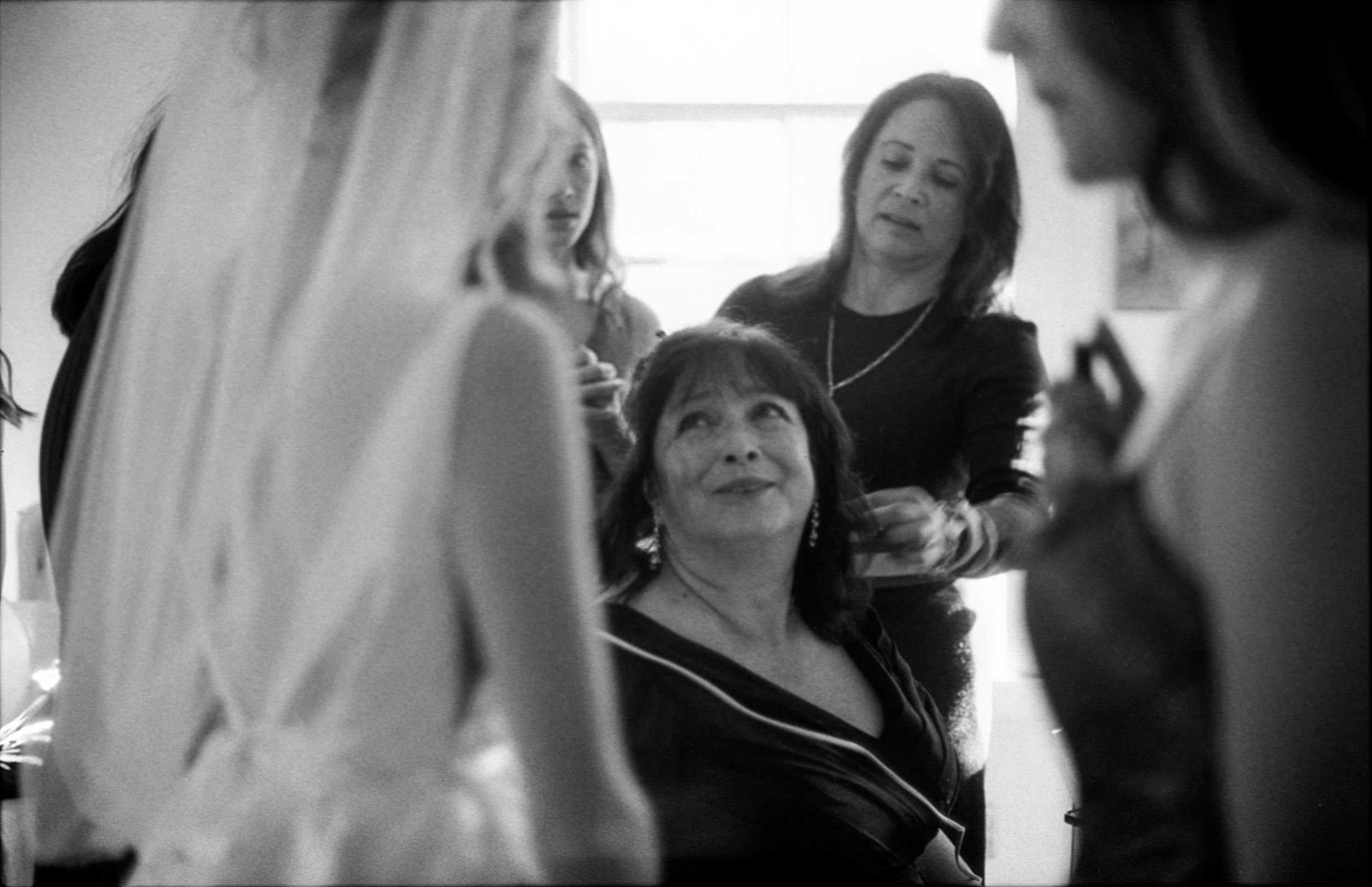 Black and white photo of women gathered around a seated older woman during bridal preparations.