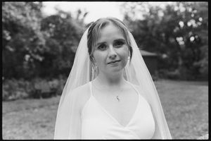 Black and white portrait of smiling bride wearing veil and delicate necklace outdoors.