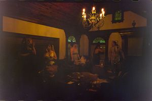 Dimly lit indoor wedding reception with chandelier and guests in elegant venue.
