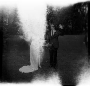 Artistic black and white film photo of bride and groom with light leak effect outdoors.