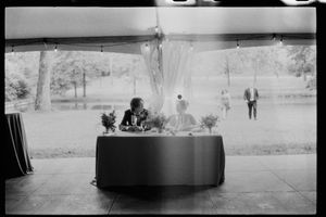Black and white film photo of bride and groom seated at sweetheart table under tent.