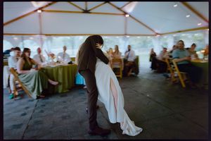Bride and groom share first dance under elegant wedding tent with guests seated at decorated tables.