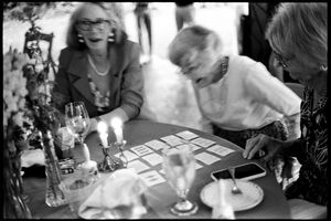 Elderly women examine place cards by candlelight at elegant wedding reception table.