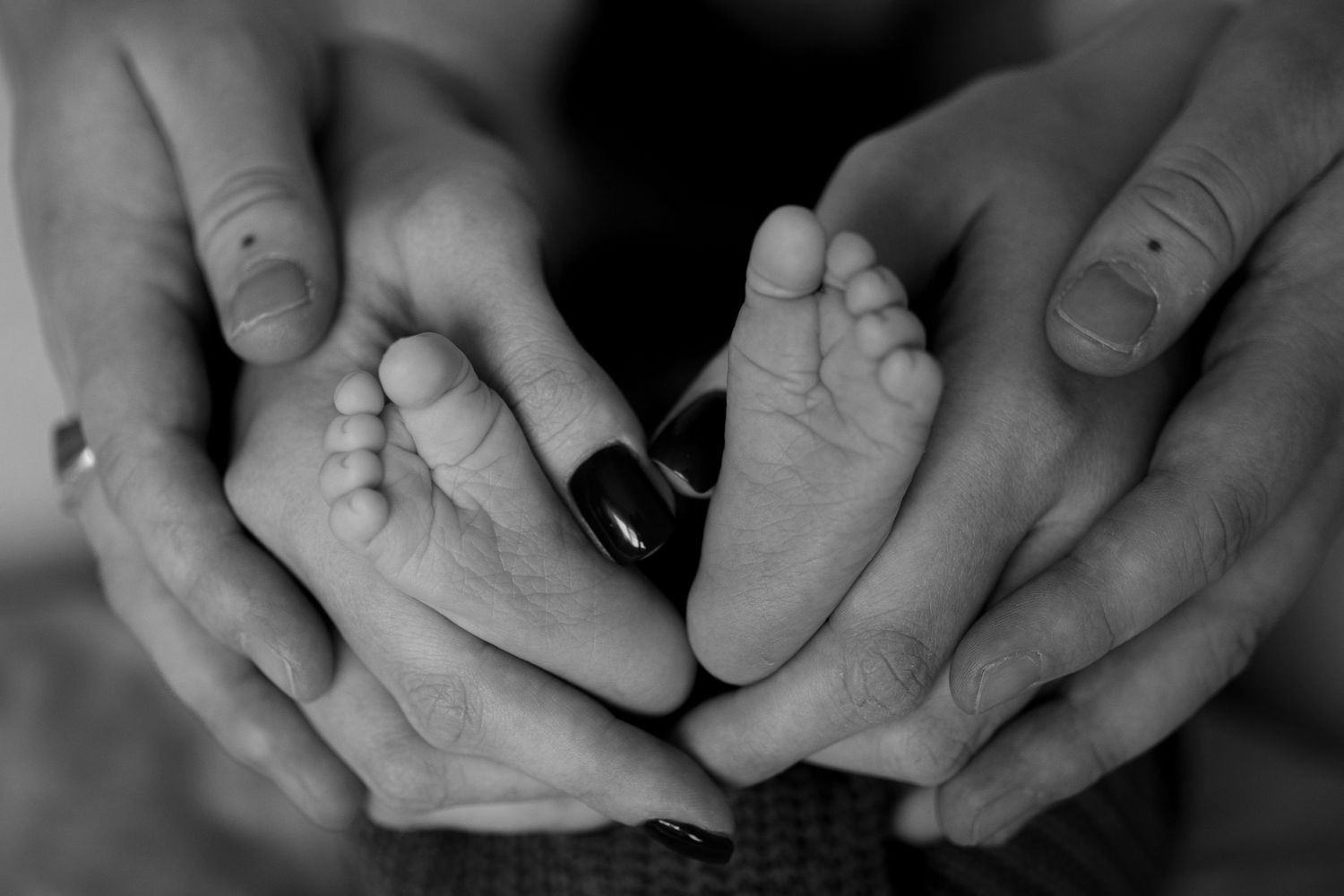 Black and white close-up series of hands tenderly holding a baby.