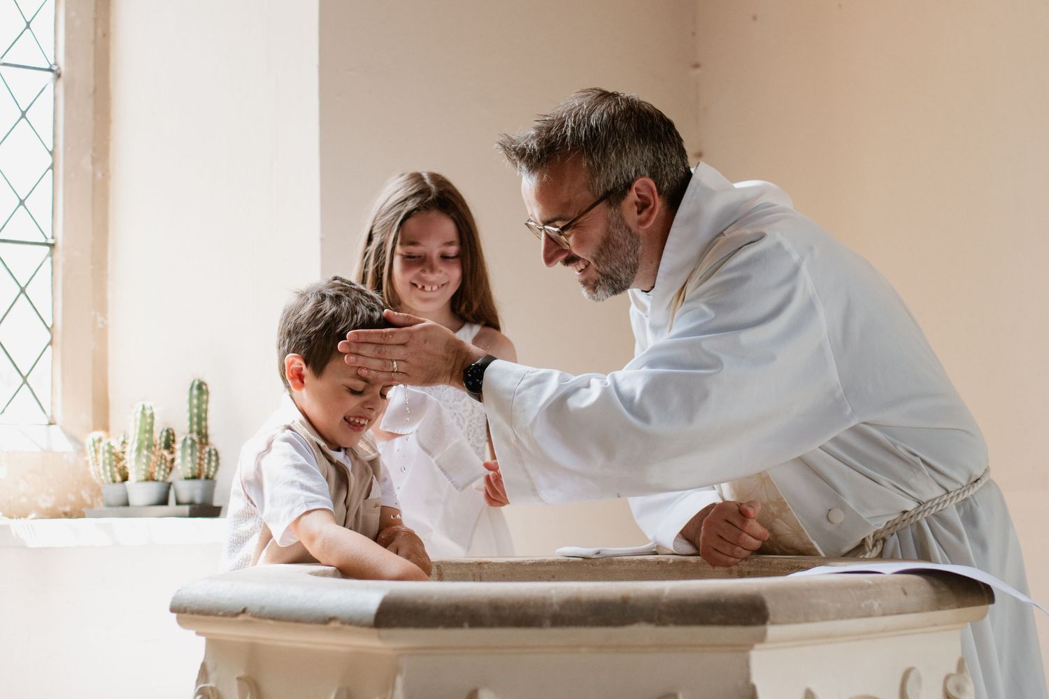 A clergy member in white vestments conducts a sacred ceremony in a sunlit church interior.