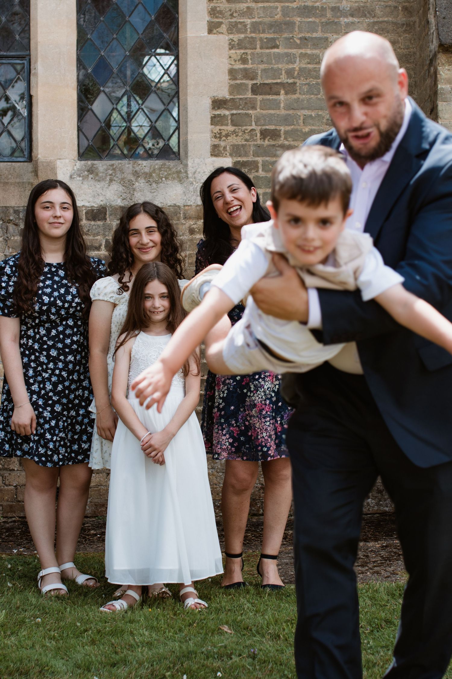 Playful family group photo sequence showing adults and children posing together outdoors by a brick wall.