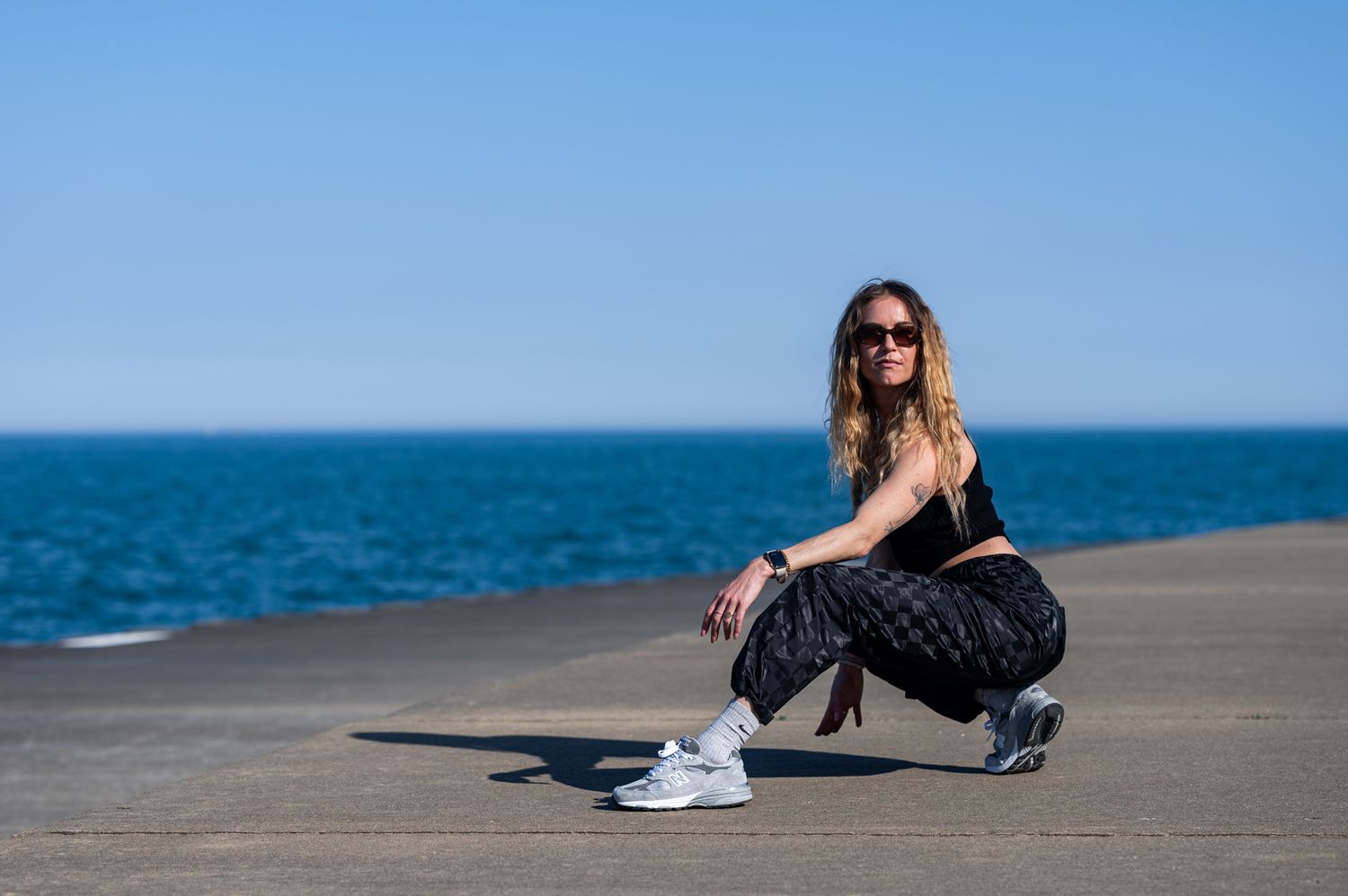 Athletic fashion photo featuring a crouching pose against a bright blue ocean backdrop.