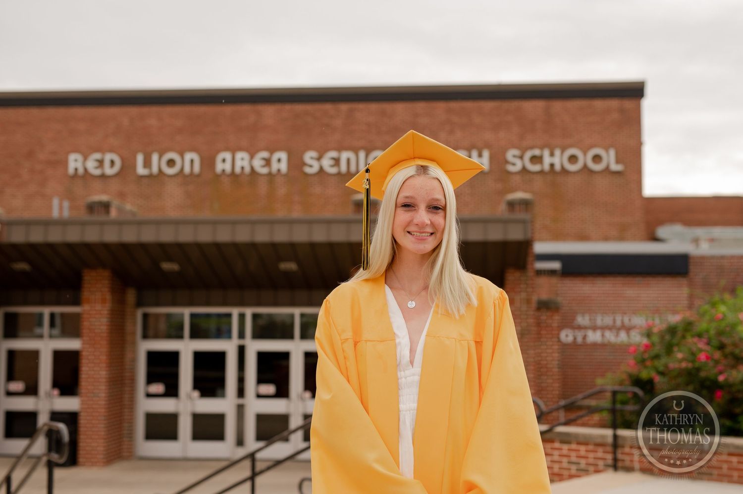 Student poses in yellow graduation regalia outside Red Lion Area Senior High School.