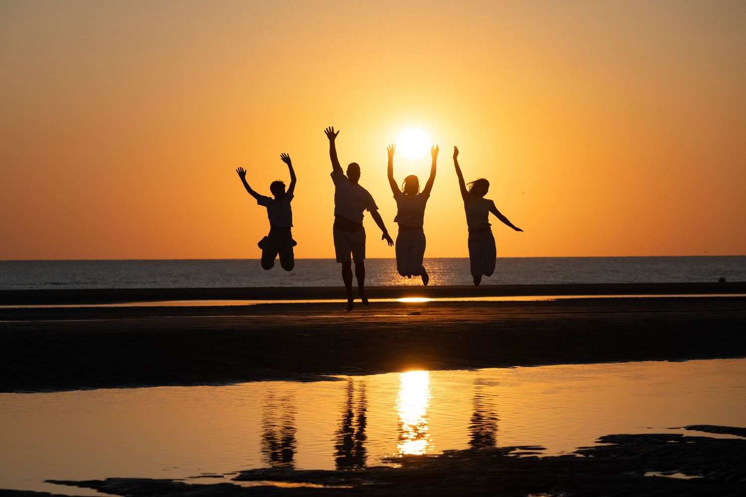 Family enjoying a playful moment together on a sandy beach with rippled sand patterns at sunset.