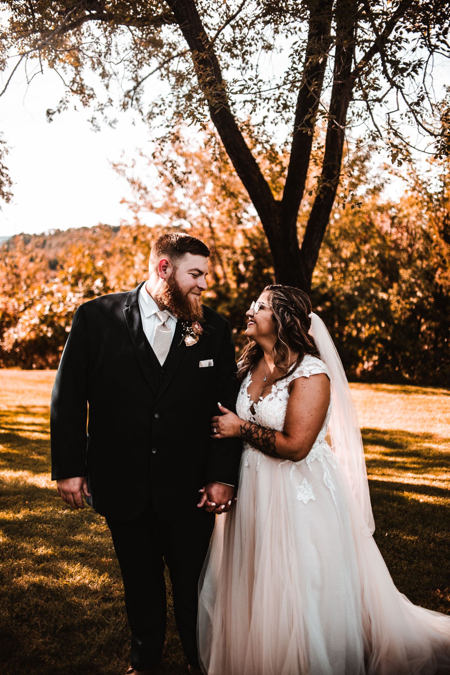 A couple shares a romantic moment together on their wedding day during golden hour beneath a tall tree in autumn.