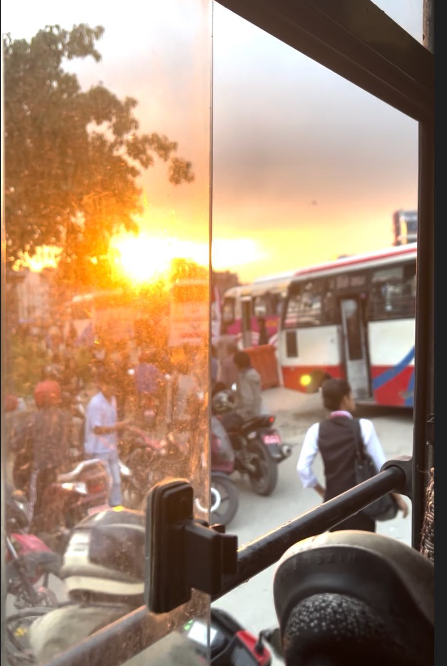 Sunset view through a window showing buses and motorcycles in a busy transportation hub.