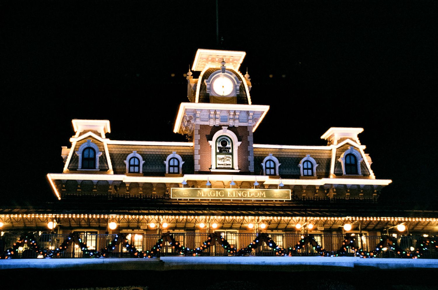 The iconic Disney World train station lit up with holiday lights against the night sky.