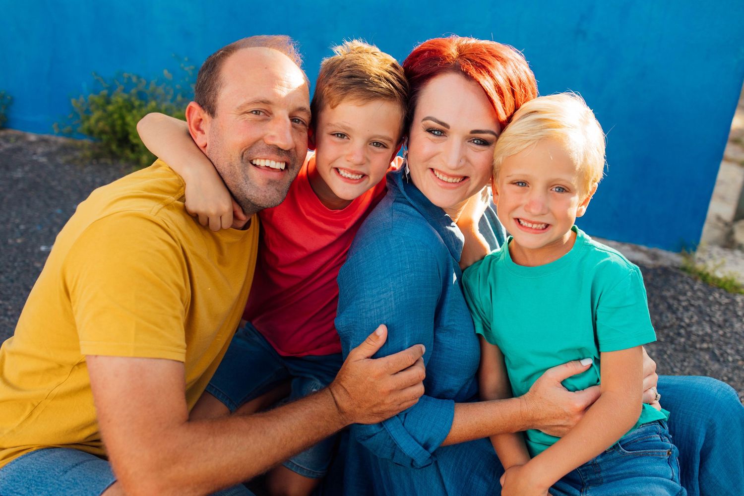 Cheerful family in colorful outfits sitting together and smiling against a bright blue background in Bo-Kaap