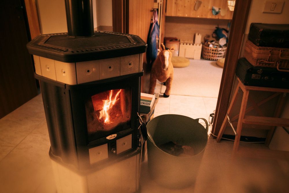 A wood-burning stove with glowing fire beside a metal bucket in a cozy dimly lit room.