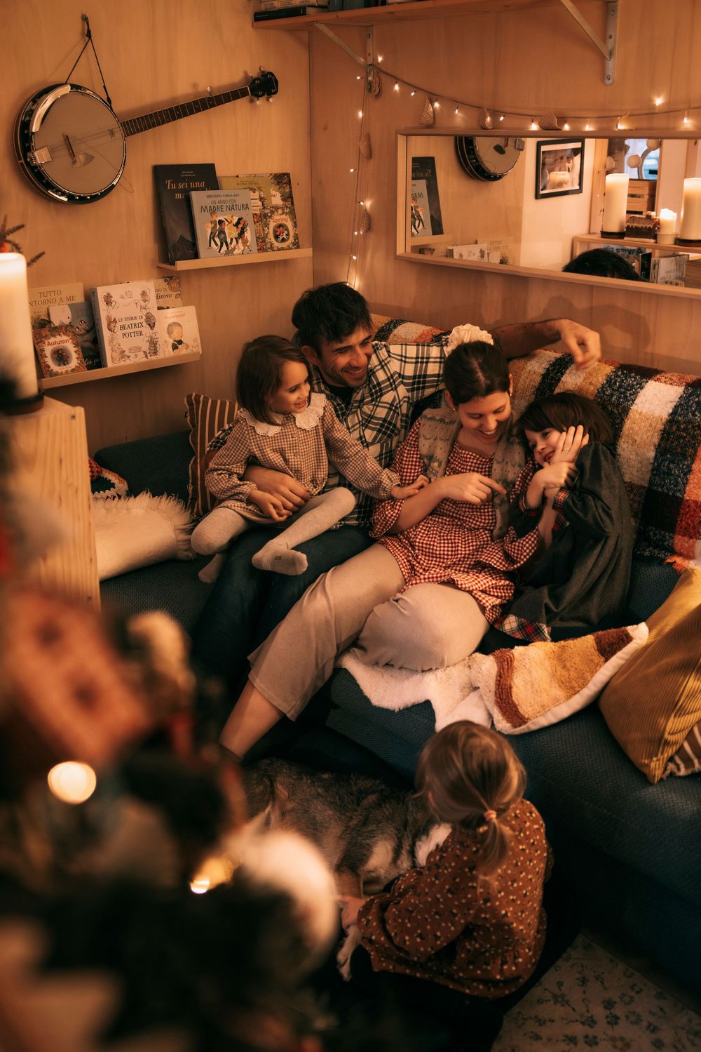 Family gathered on cozy sofa by Christmas tree in warm cabin, sharing joyful holiday moment together.