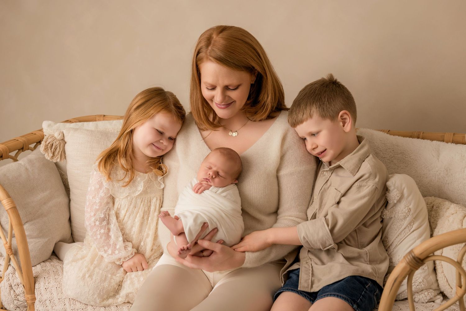 Family wearing neutral colored clothing sits together on beige couch for intimate lifestyle photoshoot.