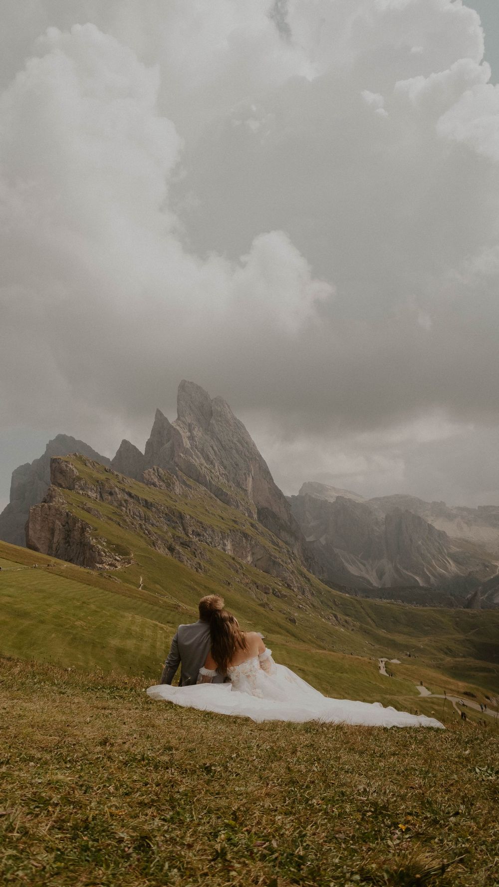 Dramatic mountain landscape in the Dolomites with jagged peaks and green meadows under moody cloudy skies.