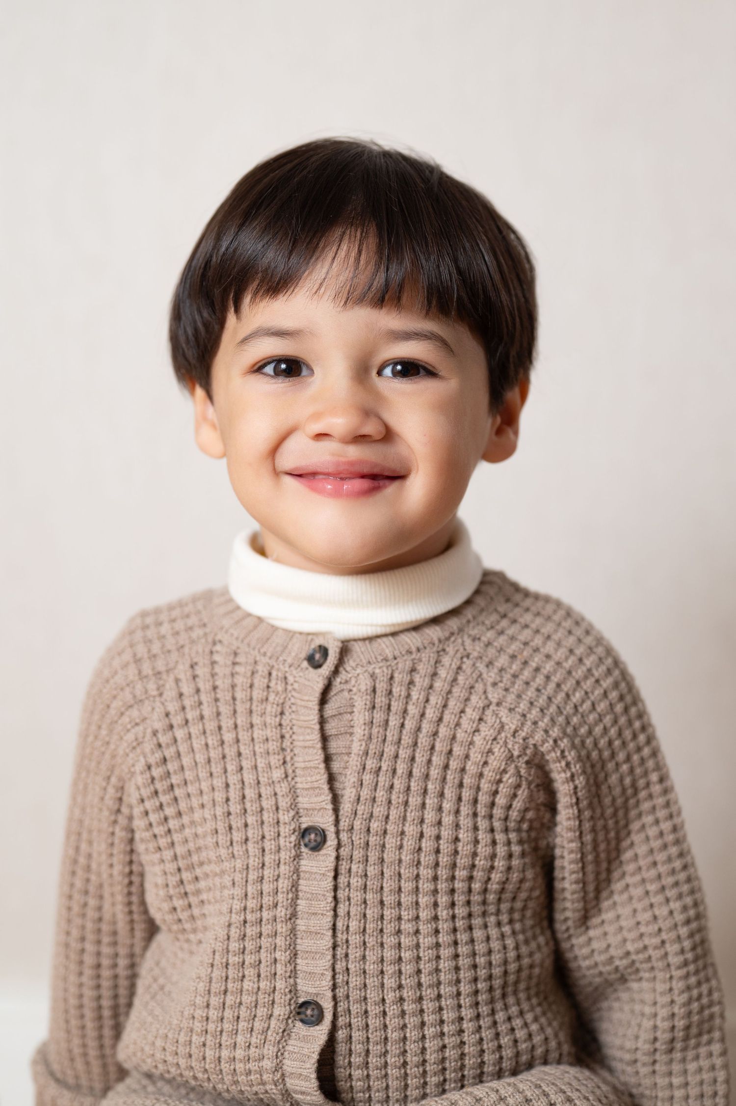 A child wearing a beige knitted cardigan sweater smiles warmly in a series of connected portrait photos.
