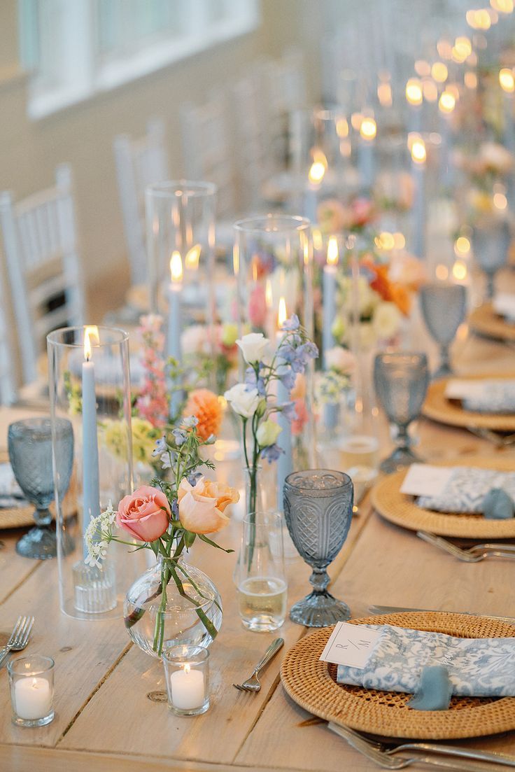 Elegant wedding table with blue glassware, candles, and colorful floral arrangements.