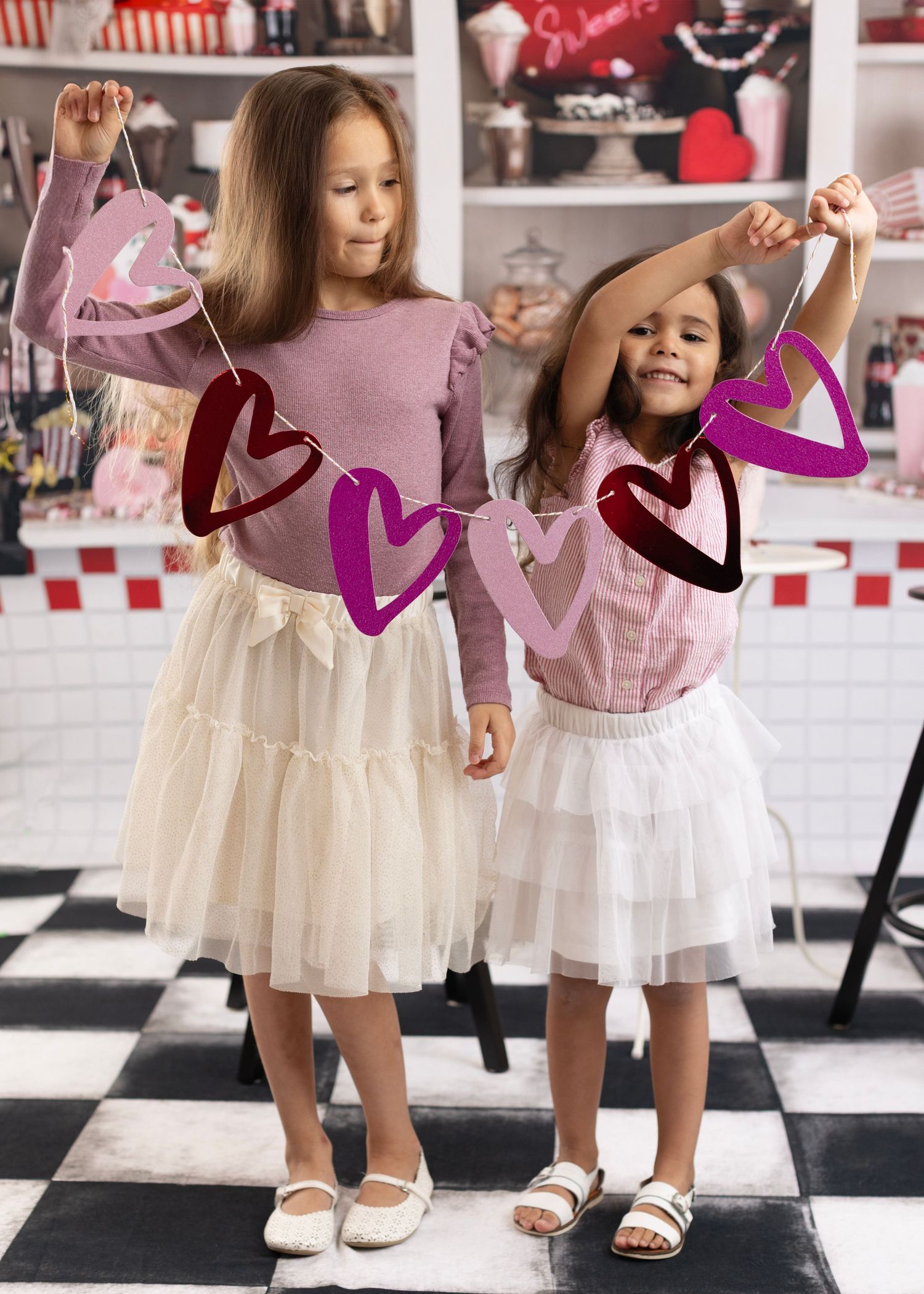 Little girls in white tulle dresses and ballet shoes twirl and dance in a vintage-styled studio with red accents.