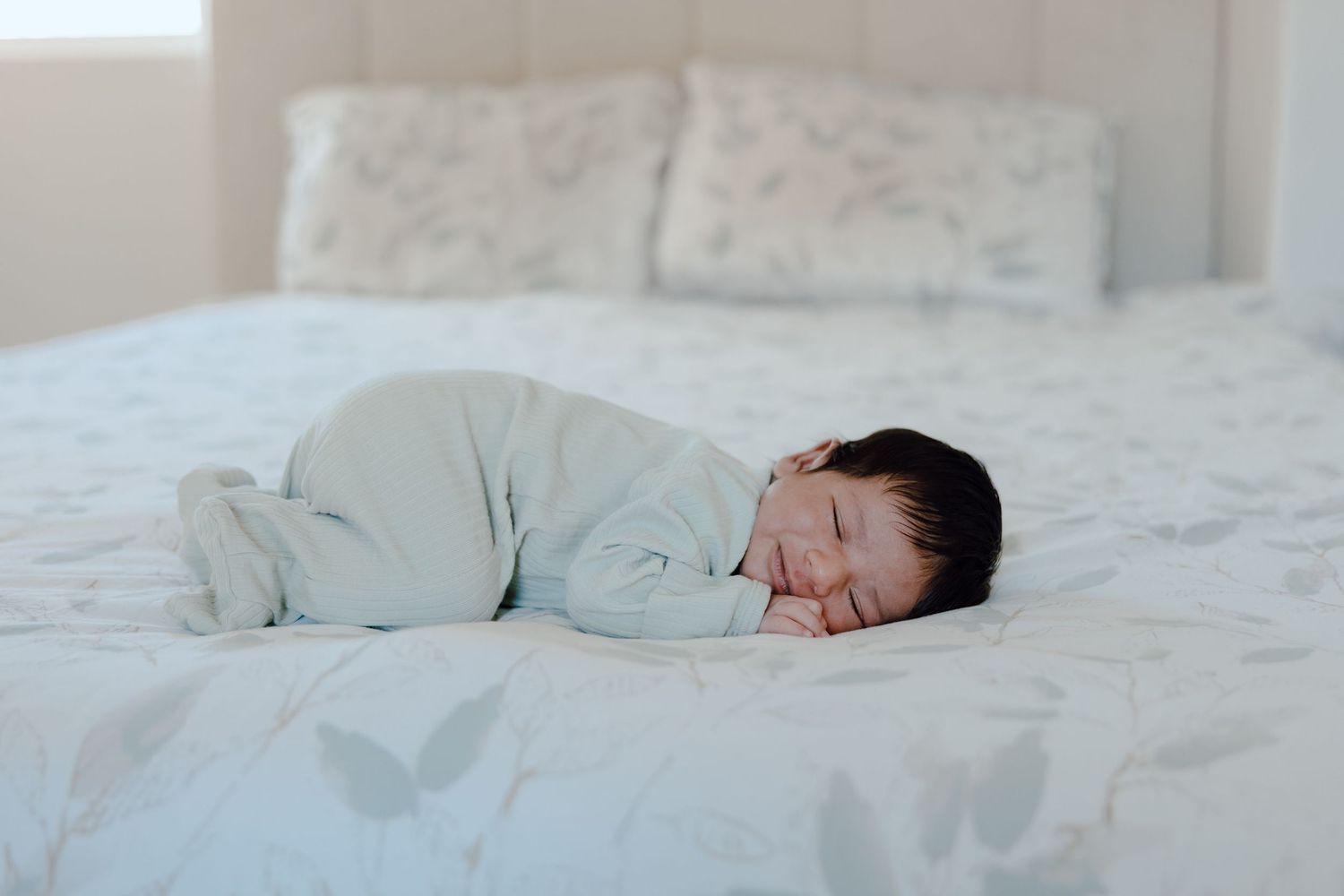 A sleeping baby wearing light green pajamas lies peacefully on white bedding.