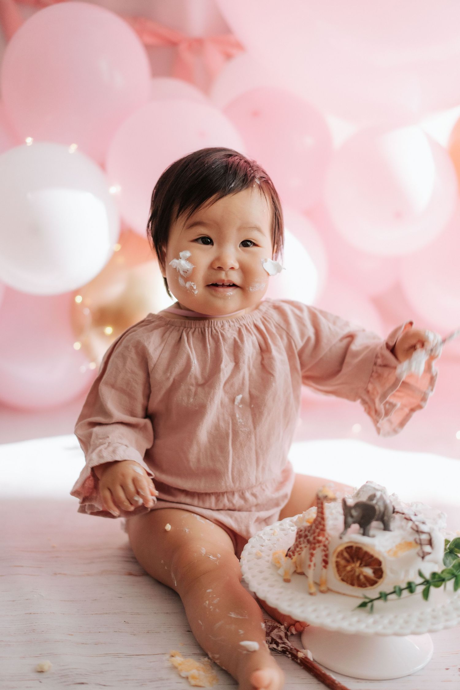 A cake smash photo session featuring a baby in pink surroundings with white frosting and decorative elements.