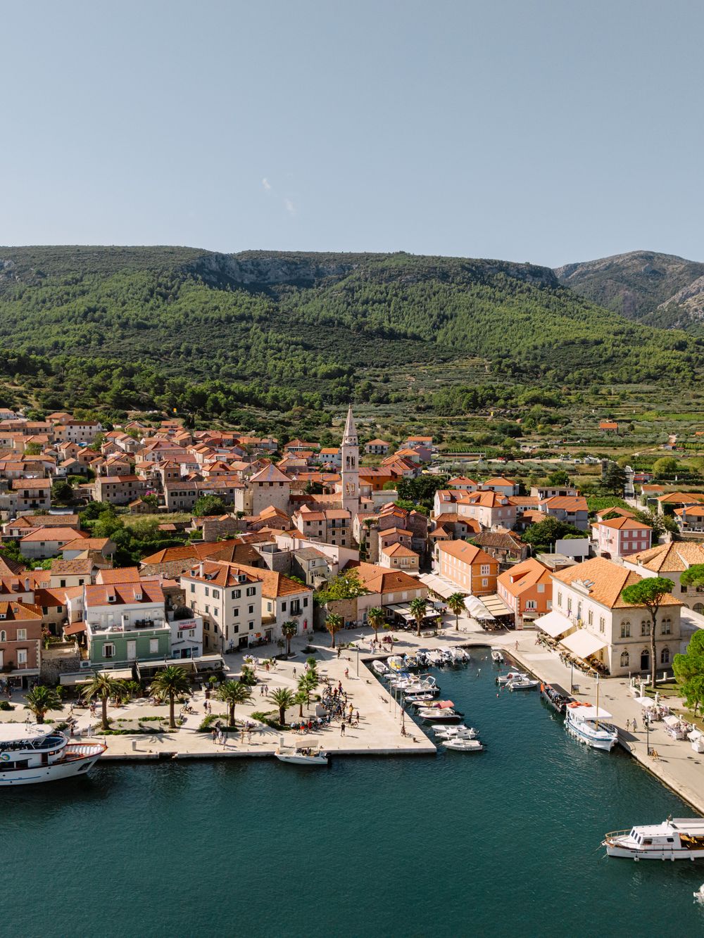 Panoramic view of a coastal Croatian village with red-roofed buildings and boats docked in the marina. Hvar, Croatia