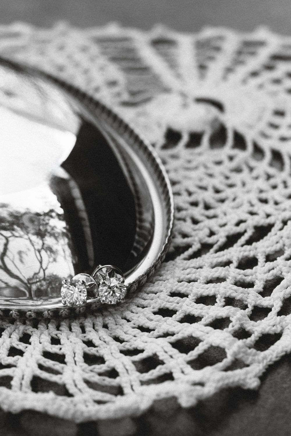 Close-up black and white photo of vintage lace doily with silver ring details creating elegant textural patterns.