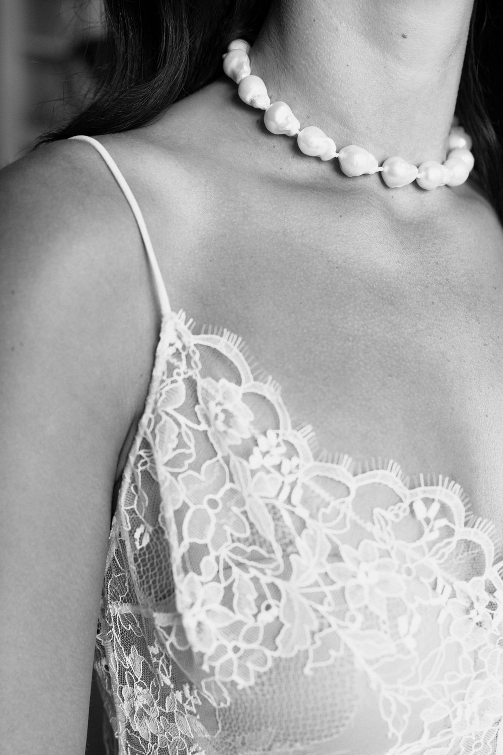 Close-up view of delicate white lace trim and pearl necklace details against a light gray background.