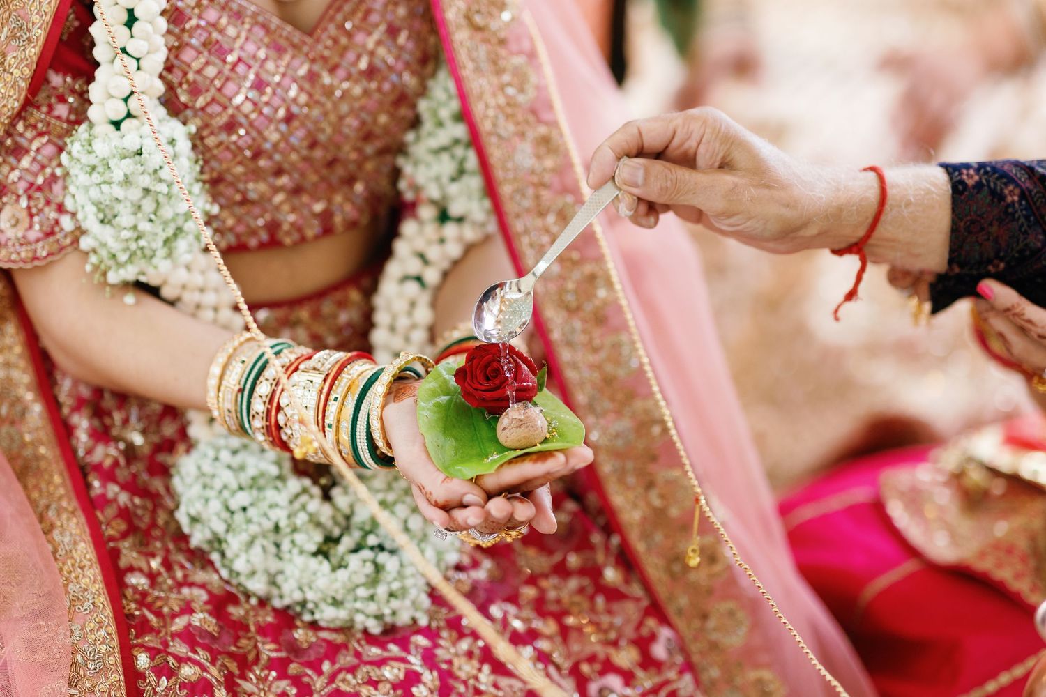 Detailed close-up of a traditional Hindu wedding ritual, showing a hand pouring water over a rose and betel leaf held by the bride.