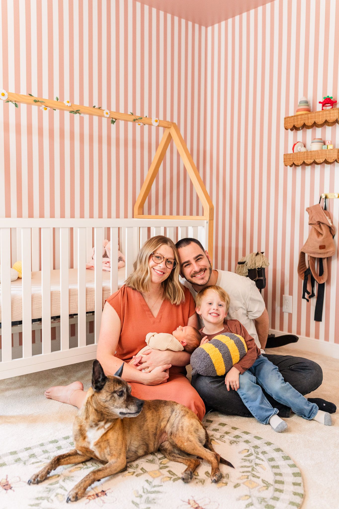 Richmond Virginia family and newborn photographer documents family snuggling new baby girl while smiling at the camera in the nursery.