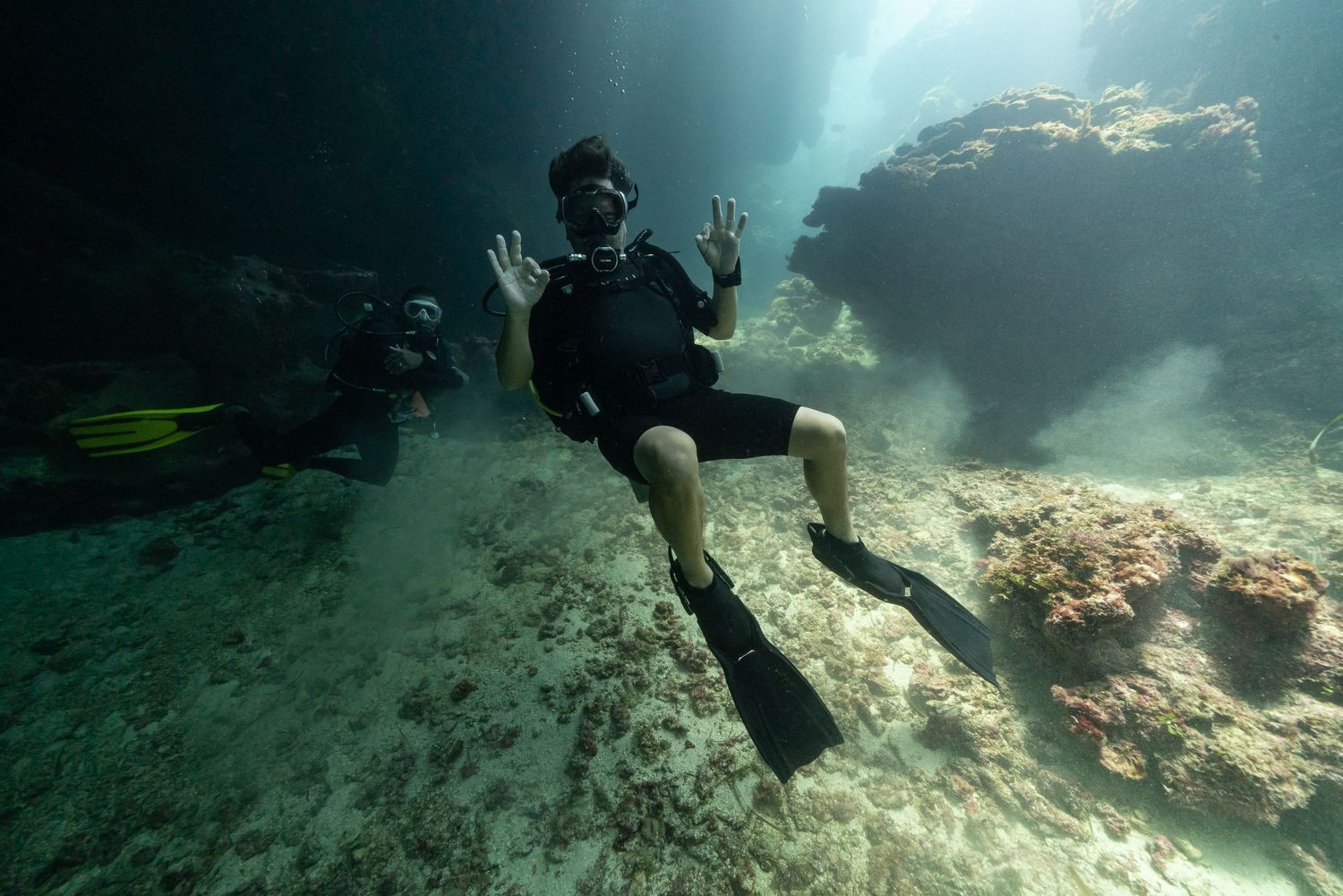 Scuba diver explores underwater coral reef formations in clear turquoise waters with dramatic lighting effects.