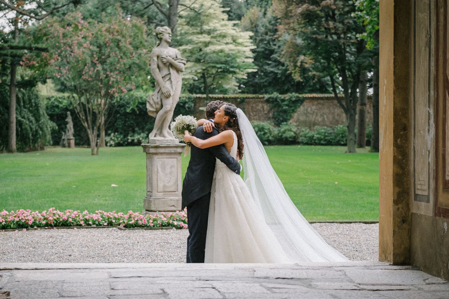 Una coppia di sposi condivide momenti romantici in un giardino con architettura classica e sculture in pietra.
