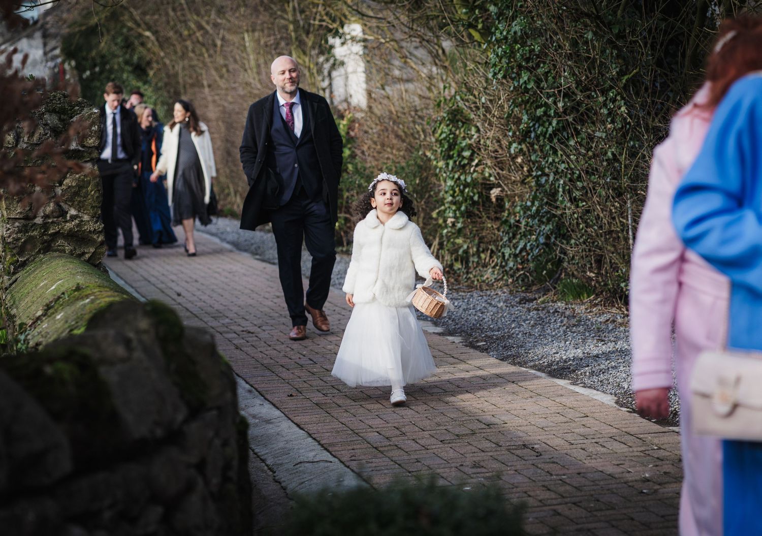 A formal event shows people walking down a brick path with a young attendant in a white dress.