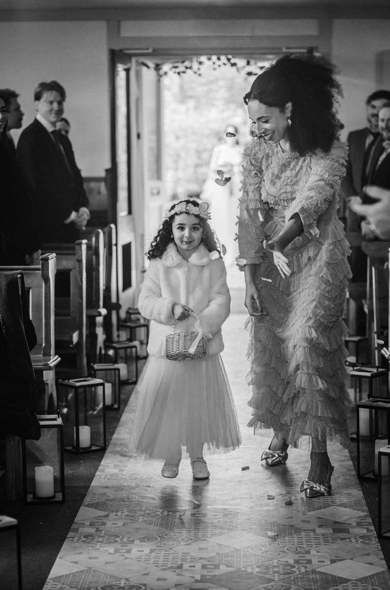 A couple in formal attire dances and twirls together on a tiled floor in black and white photography.