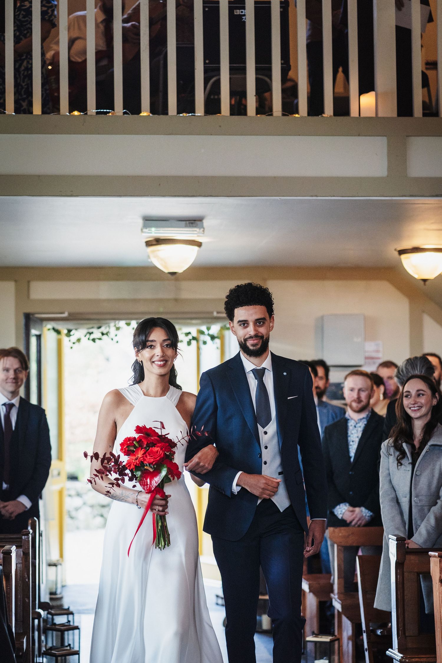 Wedding party members in formal attire line up against a light interior wall during a celebration ceremony.