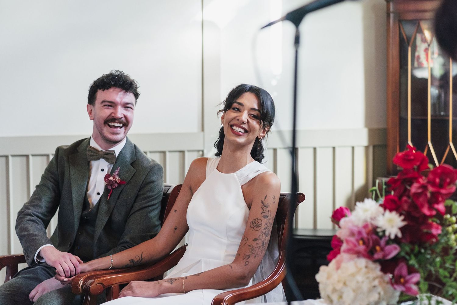 A joyful wedding couple shares a candid moment together while seated beside colorful floral arrangements.