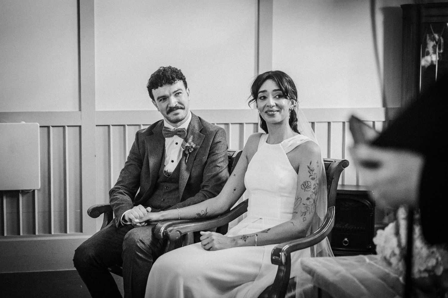 A couple sits together on a couch at a wedding reception venue while sharing a laugh.