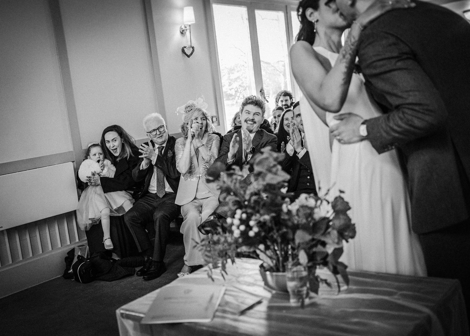 Wedding guests react emotionally while watching a ceremony in a black and white photograph.