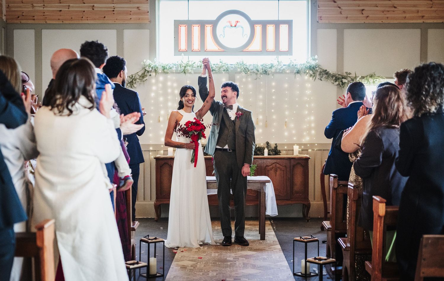 A couple stands at the altar during their wedding ceremony in a rustic venue with brick walls and twinkle lights.