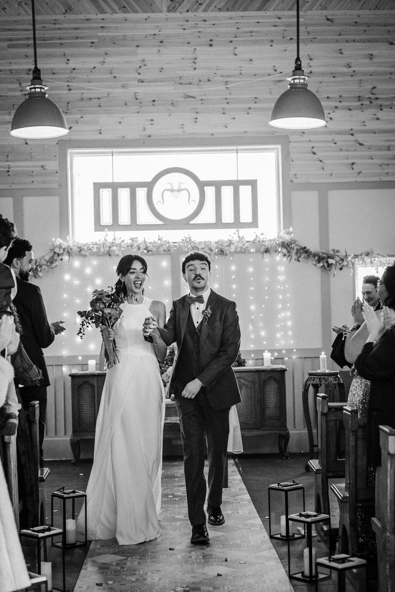 A black and white photo sequence showing a wedding ceremony in a rustic venue with wooden walls and hanging lights.
