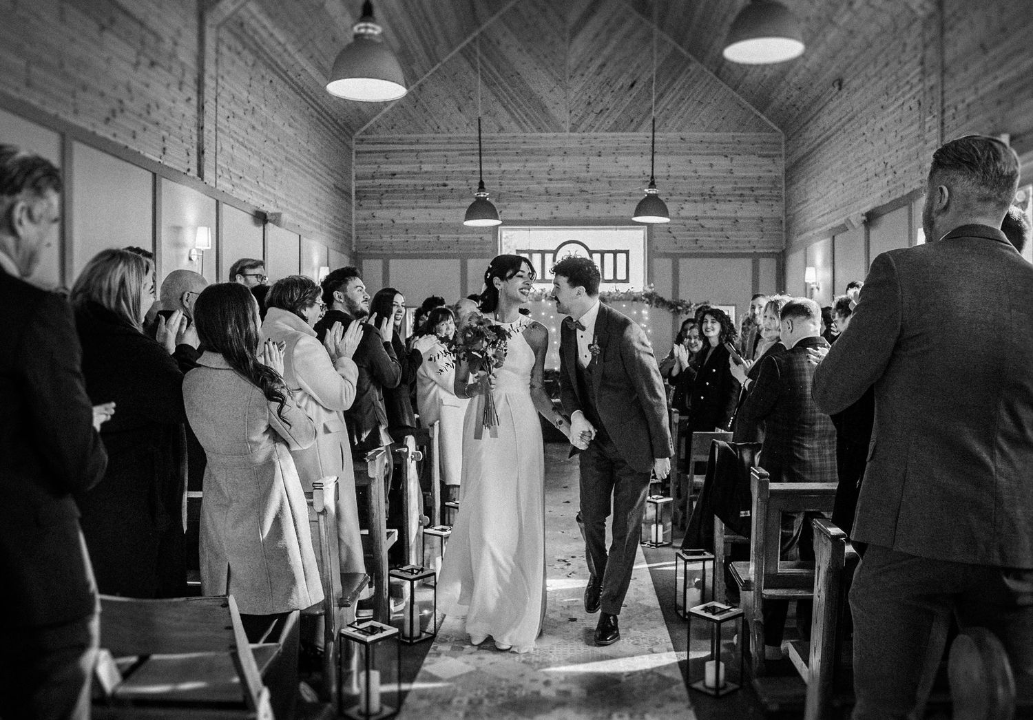 Black and white wedding reception photos show guests dancing and mingling in a rustic indoor venue.