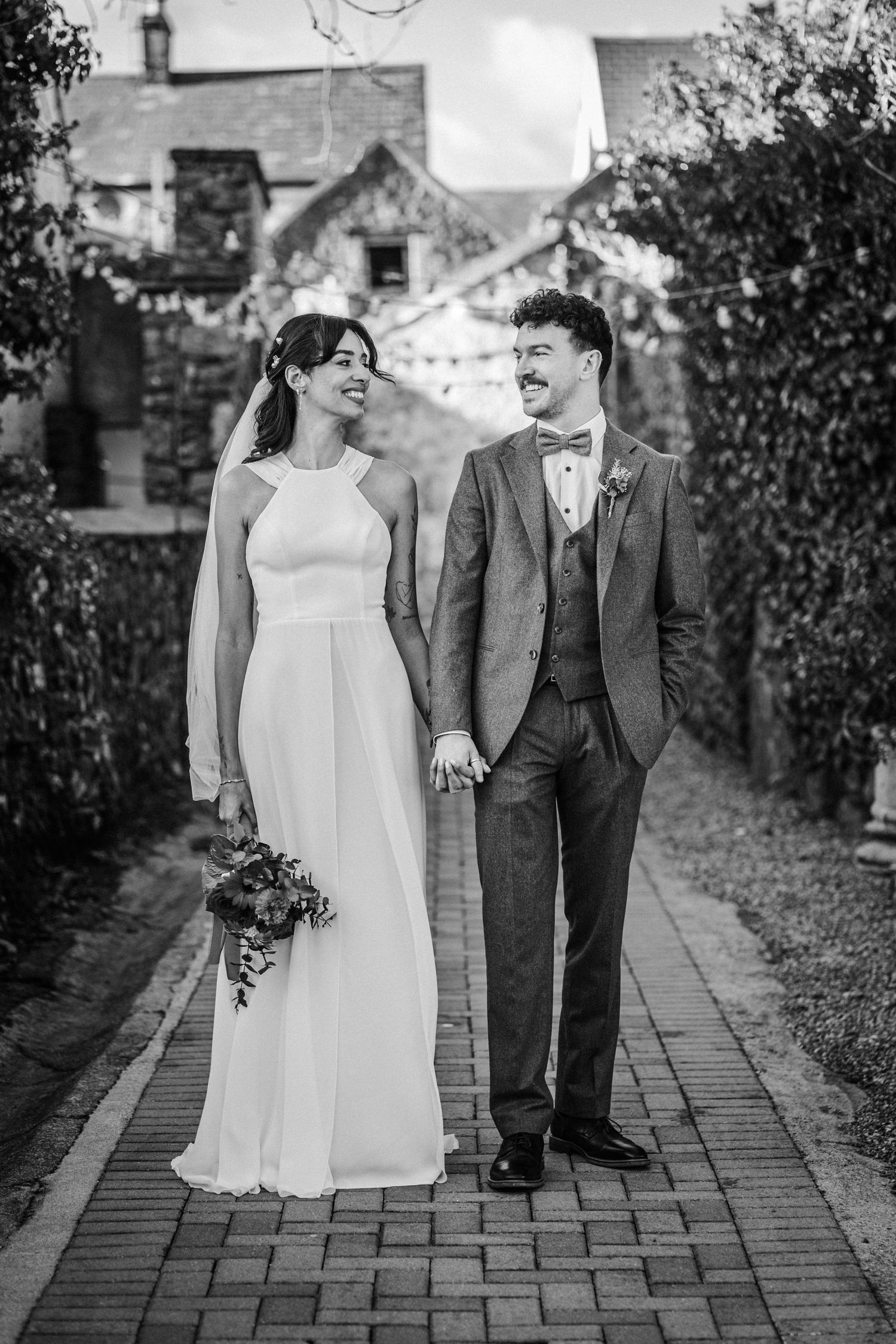 Black and white wedding photos of a couple walking together on a stone path in a garden setting.